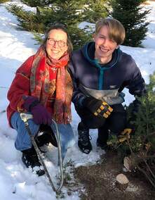 Photo of a woman and a teenager after cutting down a Christmas tree, kneeling in the snow and smiling