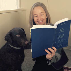 Photo of a smiling woman reading a copy of the Revised Maine Statutes while sitting on the floor next to a very cute dog who looks like she's reading too