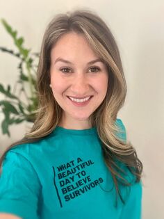 Photo of a woman smiling and wearing a teal colored t-shirt with the words 
