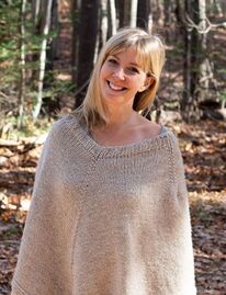 Photo of a smiling woman wearing a knit cape and standing in front of trees